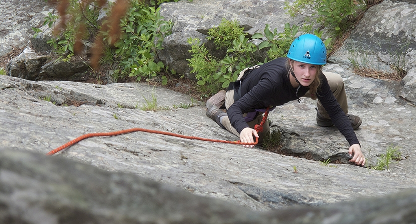 a person looks up at the camera while rock climbing on an outward bound gap year course